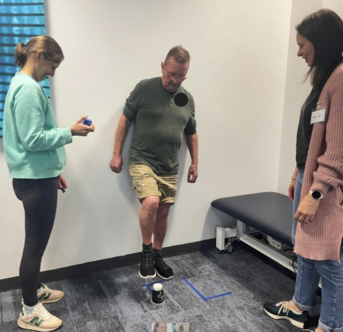 Photo of a patient taking part in a Stroke Ed rehabilitation course, watched by two therapists.