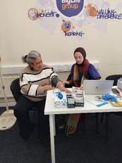 Two people sat down at a table, with one being given a health check
