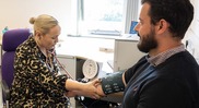 GP writing notes and taking a patient's blood pressure