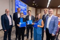 four people stood on stage in-front of the advertising 