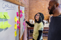 Man and woman looking at list of challenges gathered and pinned to a wall