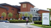 outside photo of a hospital with people walking and a sign saying wythenshawe