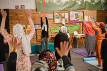 Women in a yoga class facing the instructor with their hands in the air