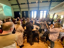 Large group of people at an event stood round tables clapping