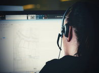 A screen viewed over the shoulder of a woman with headphones taking a call.