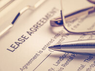 A lease agreement document with a silver pen and a pair of spectacles lying across it.