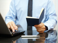 Office worker reading information from notebook and typing on laptop keyboard