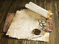 An ageing sheet of paper lying on a desk with a seal, a pair of spectacles and a scroll lying on it.