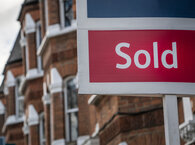 An estate agent's sold sign with a residential terrace in the background.