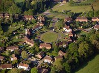 Aerial view of a suburban estate built around a central green and surrounded by woodland.