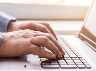 A pair of hands with the fingers resting on a laptop keyboard.