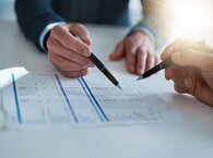 Two people examine a document lying on a desk.