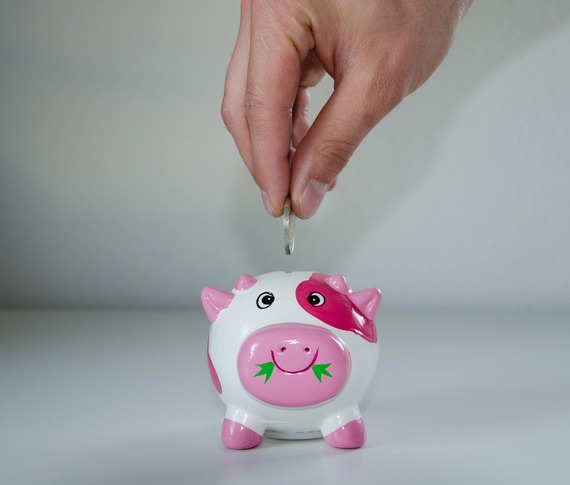 Pink and white pig money box, with coin being deposited in its back