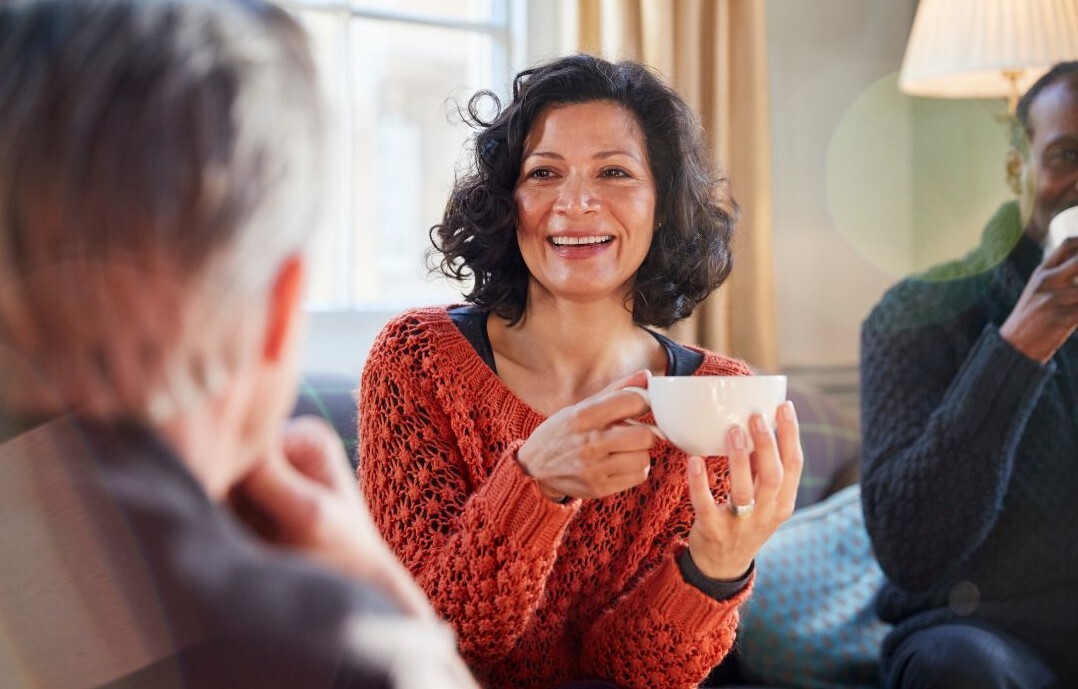 A lady sat smiling with friends, holding a cup of tea