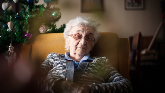 a lonely old woman sat in a chair next to a christmas tree