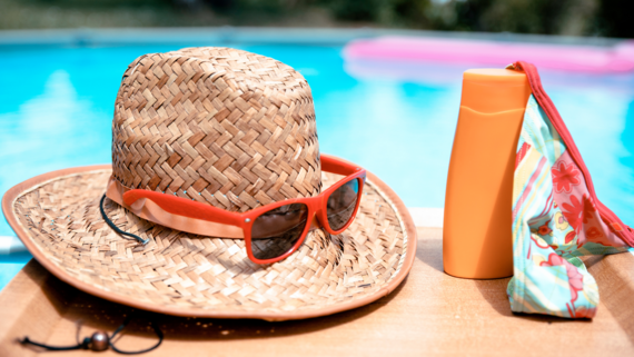 a summer hat, sunglasses and sun cream next to a swimming pool