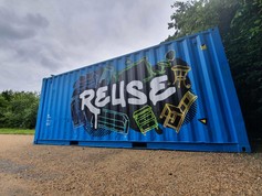 A blue container is decorated with a street-art style mural. The word Reuse is surrounded by items of furniture