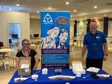 Two members of the Community Link team smiling at the welcome stand in the Wellbeing Centre