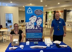 Two members of the Community Link team smiling at the welcome stand in the Wellbeing Centre