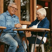 An older couple laughing over cups of coffee at a cafe
