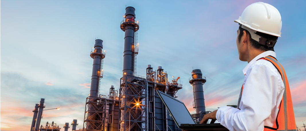 Man wearing hard hat loooking at oil refinery