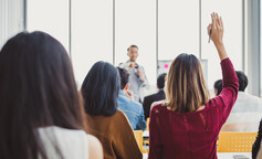 Woman raising hand to ask trainer a question in a training room