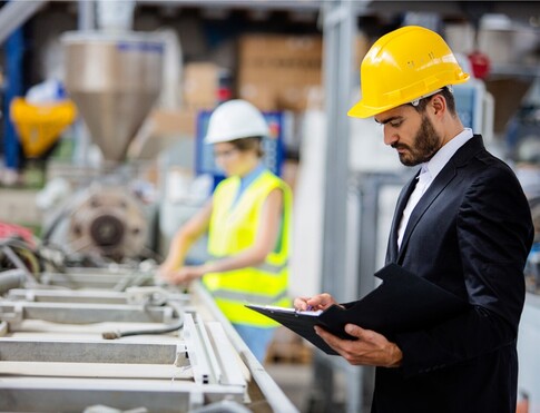 Man wearing hard hat looking at clipboard in factory