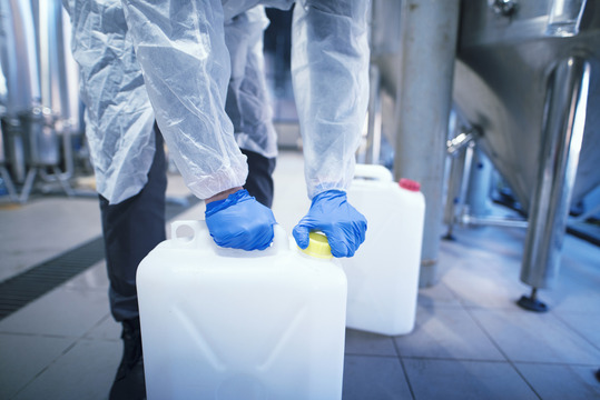 Worker wearing protective rubber gloves opening plastic can with chemicals in factory