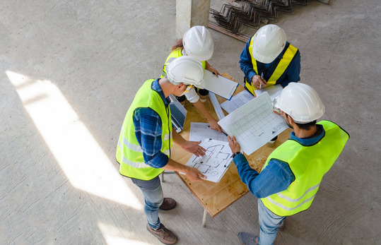 Top view of engineer, architect, contractor and foreman meeting at the construction building site with floor plan for housing project