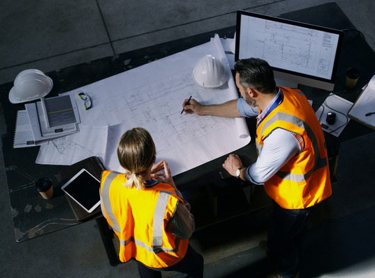 High angle shot of two engineers going over a blueprint together in an industrial place of work