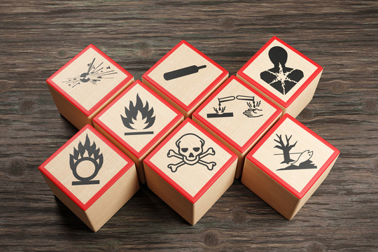 Wooden blocks showing different symbols of chemical hazard warnings on wood table.