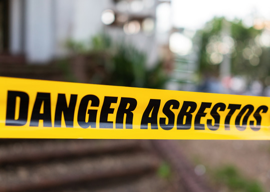 Yellow cordon tape warning of asbestos danger at the entrance to a building