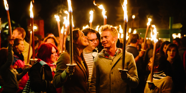 A crowd of people at night holding fire lit torches for The Tower of Light