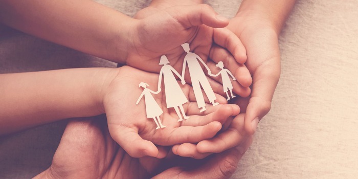 a group of hands on a pale background holding 4 paper cut ours of a group of 2 adults and 2 children.