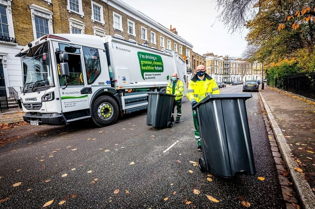 Two refuse workers collecting bins in front of a refuse truck