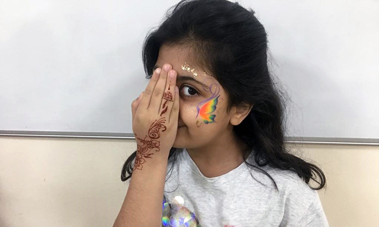Young girl with face paint and henna'd hand, holding her hand up to her face