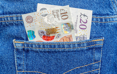 A person's back jean pocket with a ten and twenty-pound note in it.