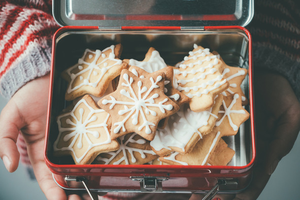 A person holding an open tin of homemade Christmas star cookies