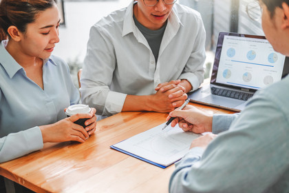 Three men and women sat around a desk looking at financial papers and a laptop discussing financial loans