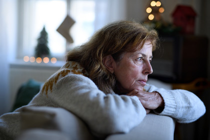 A middle-aged woman alone looking slightly down staring out of a window at Christmas time