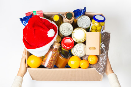 A mixed brown box of food being donated to a food bank with a red and white Christmas hat on top.