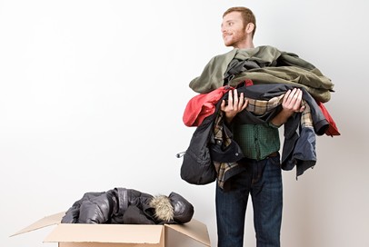 A man smiling holding lots of coats and putting them into a box ready to donate them to those in need