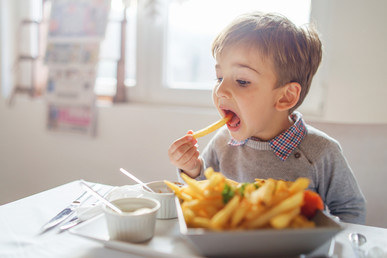 A young boy eating chips in a sunny room.