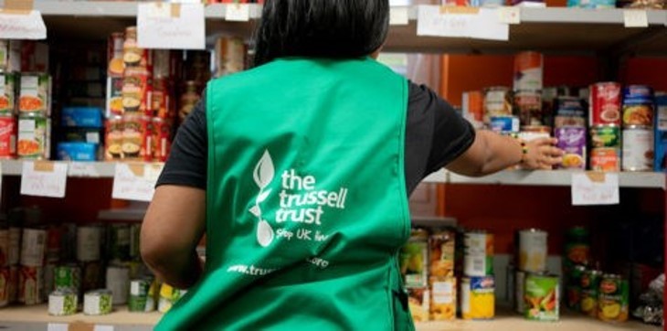 A person wearing a Trussell Trust green jacket working in a food bank