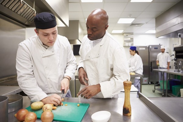 A young cook in a kitchen having a cooking lesson chopping up vegetables