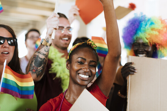 A black woman in a crowd of people of different ethnicities smiling holding gay Pride flags