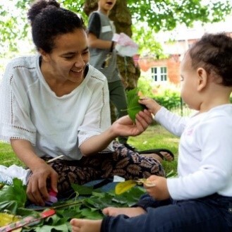 Young baby handing his mother a leaf, while sitting outside on the grass