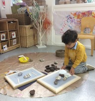 A young boy, sitting on his knees, arranging items on a frame on the floor