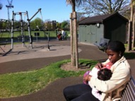A woman breastfeeding her baby on a park bench in the sun