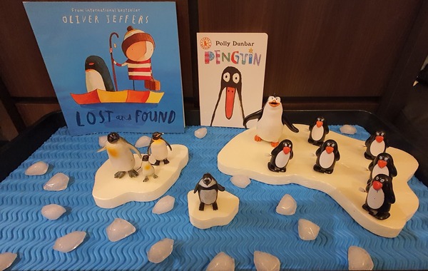 Toy penguins and books displayed with some ice